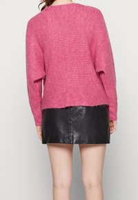 Pull rose en maille avec une finition texturée et des manches longues, associé à une mini-jupe en cuir noir. Le bas est légèrement effiloché.