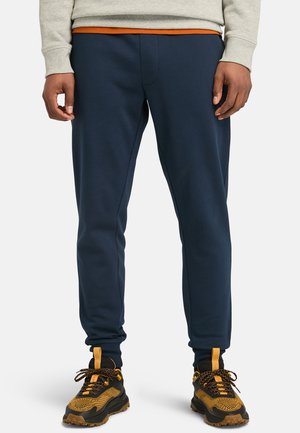 Un pantalon de survêtement bleu marine avec une taille et des poignets élastiques, fabriqué en tissu doux. Associé à des baskets noir et orange à motifs.