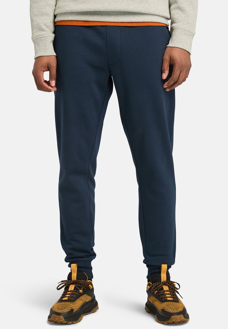 Navy blue sweatpants with elasticized waistband and cuffs, made from a soft fabric. Paired with black and orange patterned sneakers.