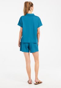 Mėlynas dviejų dalių kostiumas, turintis trumpas rankoves, apykaklę ir derančius šortus. Pagamintas iš tekstūruoto audinio; su lengvai užmaunamais sandalais.