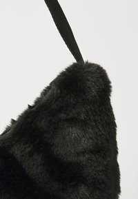Svart faux fur-veske med trekantet form, med en glatt tekstur og et svart stoffreim festet til toppen for bæring.