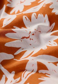 Orange fabric featuring large white floral patterns, with a smooth texture and slight wrinkling, showcasing a bold contemporary design.