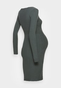 Robe en maille côtelée vert foncé à manches longues, silhouette ajustée, encolure ronde, et tissu extensible, conçue pour s'adapter à un ventre en pleine croissance.