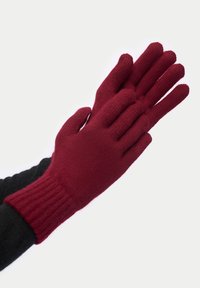 Burgundyröda stickade handskar med ribbade handledsmuddar. Har en femfingerdesign och mjuk textur, visas med en svart handske under.
