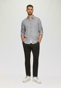 Camicia grigia button-up, pantaloni neri, sneakers chiare. Vestibilità slim, maniche lunghe, tessuto testurizzato, motivo sottile sulla camicia, colletto classico.