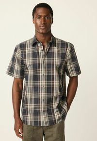 Košeľa s krátkym rukávom s károvan�ým vzorom v námorníckej modrej, hnedej a krémovej farbe. Má zapínanie na gombíky vpredu a pohodlný strih s jemným leskom v textúre látky.