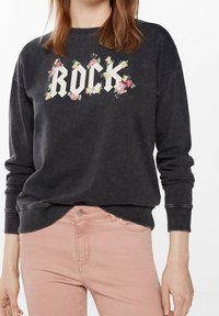 Tma šedá mikina s velkým bílým grafickým nápisem "ROCK", obklopeným květinovými vzory. Hladké manžety a lem, spárované se světle růžovými kalhotami.
