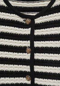 Un cardigan tricoté noir et blanc à rayures avec un col rond et des fermetures à boutons dorés, présentant un fil texturé et des rayures contrastantes.