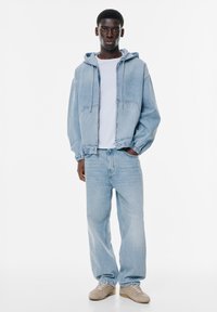 Valkoinen t-paita, taivaansinisestä denimmistä valmistettu huppari, jossa on nauhakuulokkeet, ja vastaavat vaalean siniset leveälahkeiset farkut sekä beige kengät. Sileä rakenne.