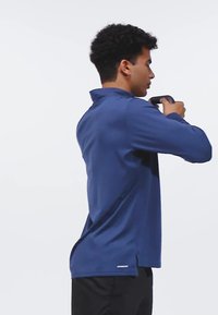 Donkerblauwe lange mouwen shirt met een kraag, zijsplitten aan de onderkant en een getailleerd ontwerp, gedragen door een persoon die een zwart voorwerp vasthoudt.