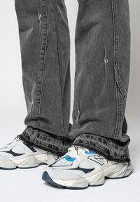 Housut harmaasta denimestä, joissa on risat helmat ja hopeiset yksityiskohdat, yhdistettynä tukeviin harmaan ja sinisen sävyisten sneaker-kengiin, joissa on tekstuuri.