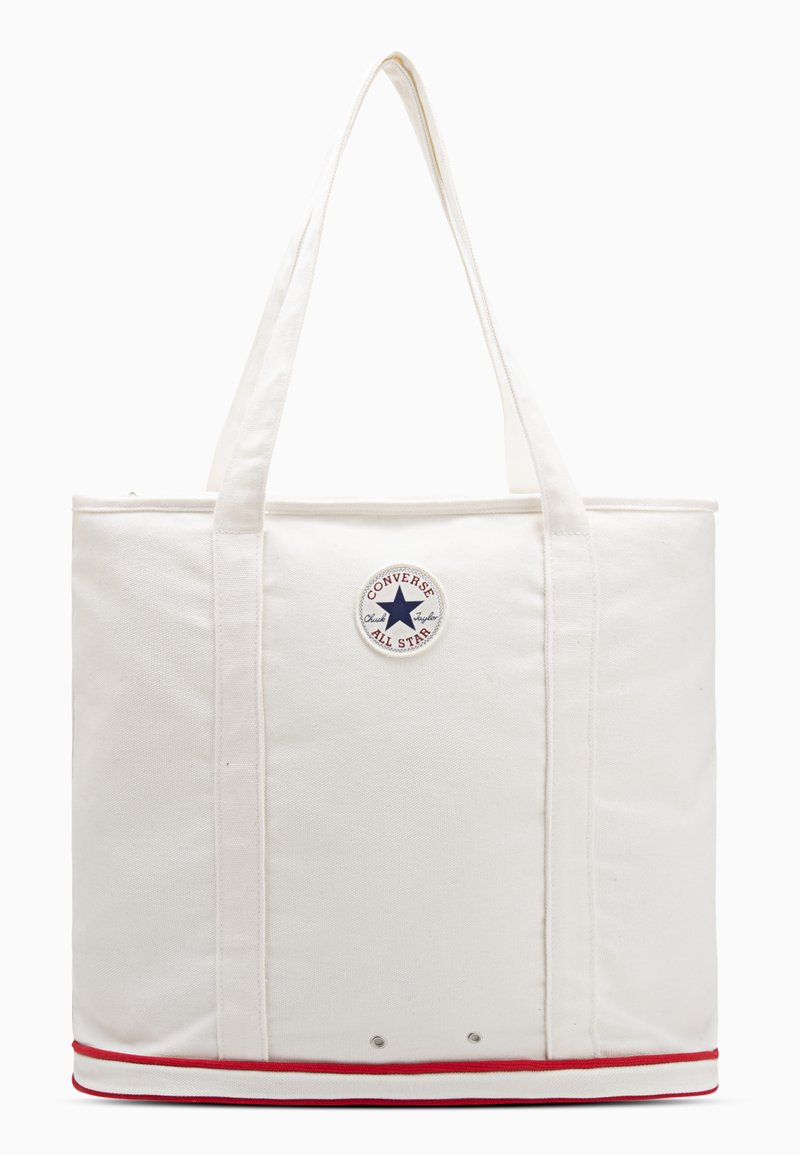 Witte canvas tote bag met twee stevige handvatten, voorzien van een rond zwart en blauw sterrenlogo en een onderkant met rode strepen. Zachte textuur.