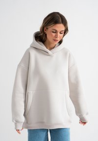 Hellgrauer, übergroßer Kapuzenpullover aus weichem Stoff, mit einer großen Tasche und verstellbarem Kordelzug an der Kapuze. Lange Ärmel mit gerippten Bündchen.