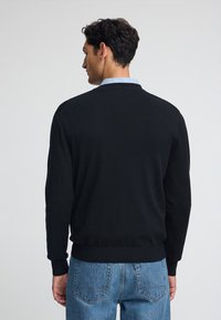 Maglione nero lavorato a maglia con colletto tondo, polsini e vita a coste, abbinato a jeans in denim blu chiaro.