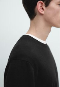 Schwarzer Pullover mit geripptem Ausschnitt und Schulternaht-Details, mit glatter Textur und eng anliegendem Design.