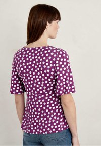 Fioletowa bluzka z krótkim rękawem w białe kropki, z okrągłym dekoltem i dopasowanym talią, wykonana z teksturowanej tkaniny.