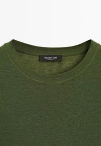 T-shirt vert olive à col rond avec une étiquette noire au col indiquant "Massimo Dutti, Fabriqué en Chine."