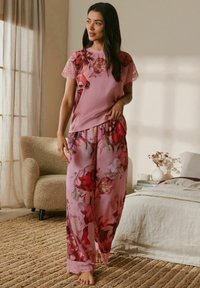 Ružová kvetinová súprava pyžama s čipkovými detailmi na rukávoch a lemoch, pozostávajúca z voľných, padavých nohavíc a priliehavého topu s zaobleným lemom.