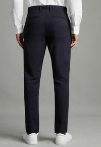 Chinos navy à coupe slim, en tissu lisse, avec deux poches arrière et passants de ceinture, assortis à des baskets blanches.