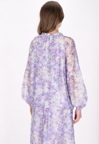 Bluză transparentă cu model floral, cu mâneci ample. Culori liliace și pastelate. Decolteu volanat și design fluid.
