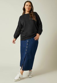 Svart tröja med spettsdetaljer på ärmarna, ihop med en medellång blå denimkjol med knappar fram och vita sneakers.