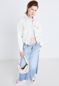 Bela skrajšana denim jakna čez belo majico, v kombinaciji s svetlo modro maksi krilo. Drži kremasto torbico; srebrne sandale.