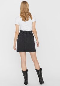 Falda de mezclilla negra con una cinturilla elástica con volantes, dos bolsillos traseros y una silueta recta. Combinada con una camiseta blanca y botas negras.