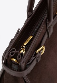 Bruin suède handtas met leren accenten, ritssluiting, gouden hardware en een sleutelhangerbevestiging.