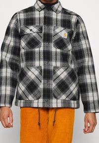 Grau und schwarz karierte Flanellhemdjacke mit langen Ärmeln, Brusttaschen, Druckknöpfen und Kordelzugsaum, aus weichem Stoff hergestellt.