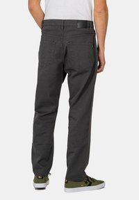 Gray cotton trousers with a straight fit, featuring two back pockets and a leather patch on the waistband. Worn with green sneakers.
