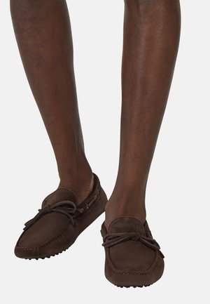 Zapatos de mocasín de ante marrón con punta redondeada, detalle de lazo en el frente y suela de goma texturizada para mayor tracción.