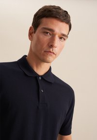 Navy polo z kołnierzykiem, krótkimi rękawami i trzema guzikami. Materiał wydaje się teksturowany i miękki, odpowiedni do codziennego noszenia.