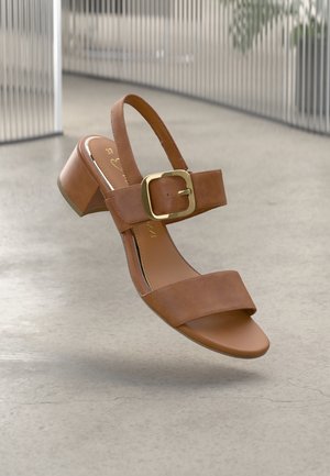 Brune læder hælesandal med en bred rem og en guld spænde detalje. Har en mellemstor blokhæl og en glat, mat finish.