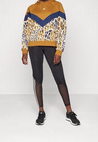 Mikina s kapucí ve hořčicové barvě s námořnickým pruhem, dolní část s leopardím vzorem; kombinováno s černými legínami a sportovní obuví.
