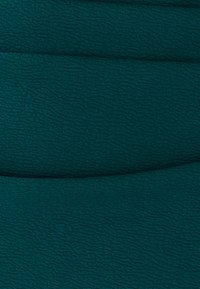 Tyrkysově modrozelená tkanina s vroubkovaným vzorem, zobrazující měkký, mírně vyvýšený povrch. Materiál vypadá hebce a odolně.