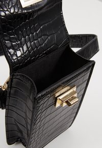 Svart handväska med krokodilmönster, guldfärgad lås och texturerad yta. Insidan är fodrad med svart tyg, öppen toppdesign.