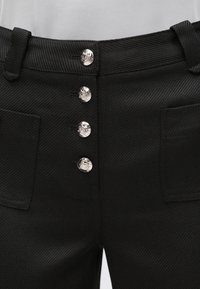 Μαύρο παντελόνι με υφή υφάσματος σε σχέδιο ψαροκόκκαλο, πέντε ασημένια κουμπιά στη μέση και δύο μπροστινές τσέπες.