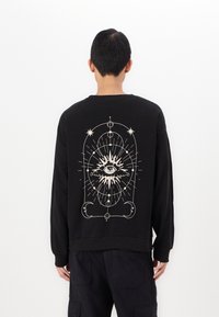 Zwarte sweatshirt van katoen, met een grote witte grafische afbeelding op de achterkant met een oog en hemelse elementen. Lange mouwen, casual pasvorm.