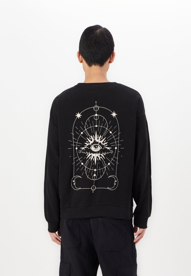 Zwarte sweatshirt van katoen, met een grote witte grafische afbeelding op de achterkant met een oog en hemelse elementen. Lange mouwen, casual pasvorm.