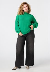 Groen gebreide trui met een col, gecombineerd met losse zwarte spijkerbroeken en enkellaarsjes met slangprint. Gestructureerde stof en een ontspannen pasvorm.