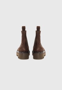 Botas de tobillo de ante marrón con una suela de plataforma gruesa, que presentan una textura suave, paneles laterales elásticos y lengüetas en la parte trasera.