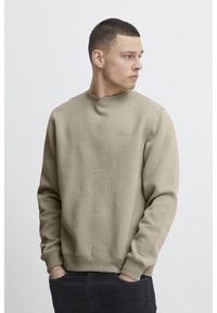 Sudadera beige con cuello redondo, puños y dobladillo acanalados. Branding sutil en el pecho. Textura suave con un diseño sencillo.