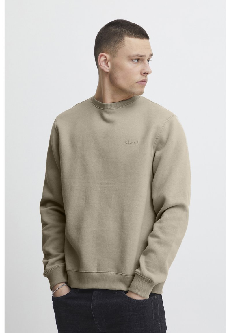 Sudadera beige con cuello redondo, puños y dobladillo acanalados. Branding sutil en el pecho. Textura suave con un diseño sencillo.