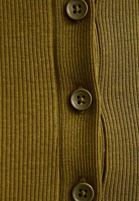 Płócienko w oliwkowej zieleni z pięcioma okrągłymi guzikami na froncie, teksturowana powierzchnia i pionowe linie tworzące subtelny wzór.