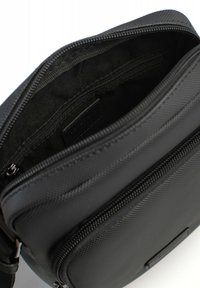 Borsa nera in nylon con una superficie testurizzata, dotata di apertura con zip e di una tasca interna con etichetta. Design compatto e strutturato.