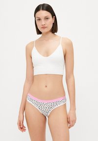 Bralet din bumbac alb cu bretele subțiri. Chiloți albi cu buline negre și un tiv elastic roz. Design simplu, confortabil.