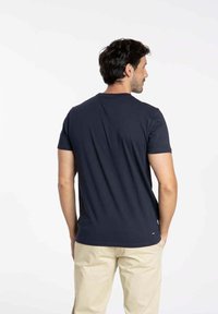 T-shirt bleu marine à col rond en mélange de coton, doté de manches courtes et d'un ourlet droit, porté avec un pantalon de couleur claire.