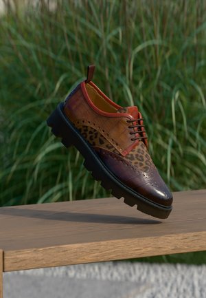 Chaussure en cuir marron avec imprimé léopard et semelle noire épaisse flottant au-dessus d'un banc en bois avec un fond d'herbe verte.