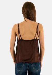 Camisola di raso marrone con dettagli in pizzo, spalline regolabili e vestibilità morbida. Indossata con jeans di denim blu, mette in risalto il design sul retro.