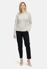 Hellgrauer, flauschiger Strickpullover mit rundem Ausschnitt und geripptem Saum, kombiniert mit schwarzen, schmal zulaufenden Hosen und beigen High Heels.